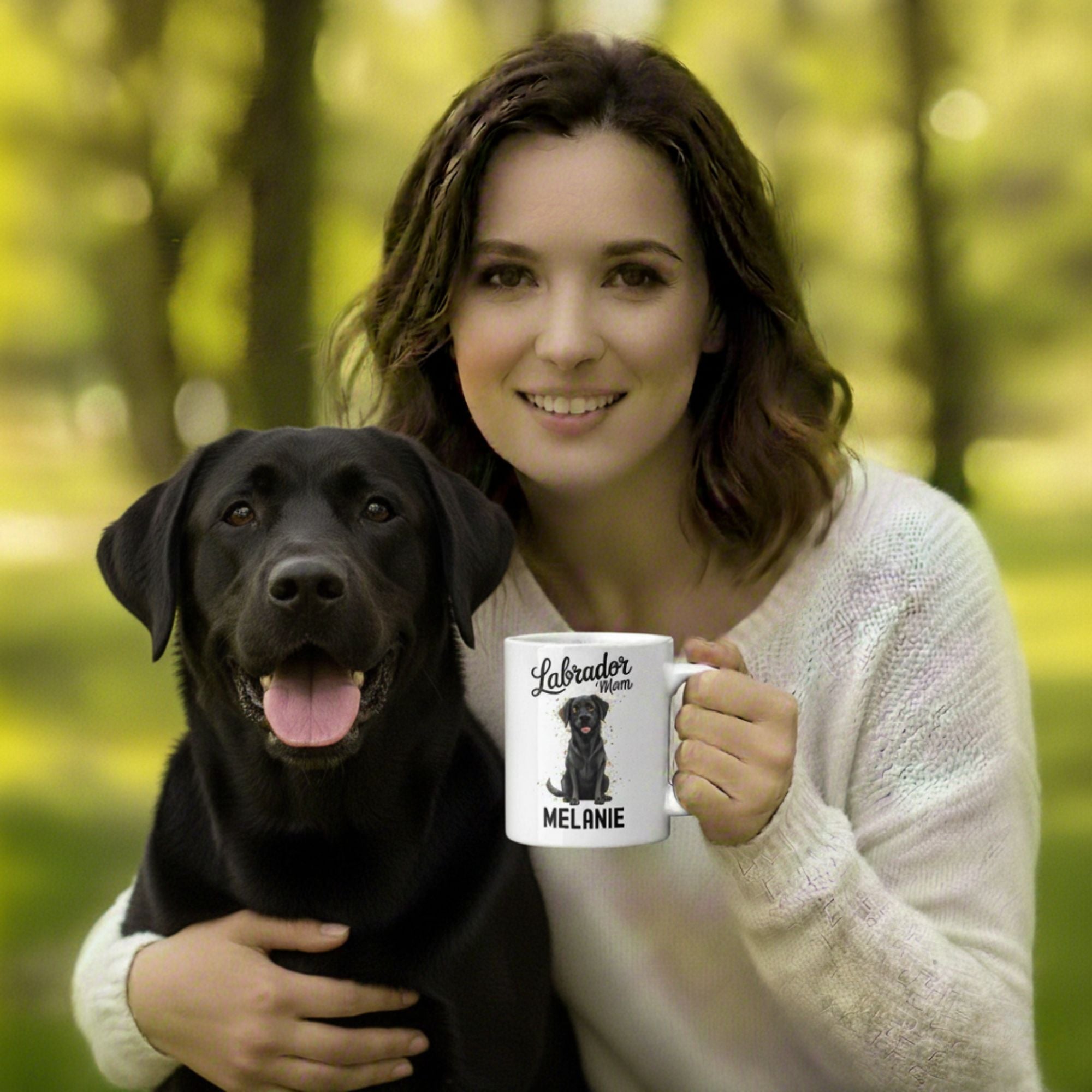Woman holding a black dog and a mug with a Labrador illustration in a forest setting